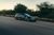 A car is driving down a road with trees in the background.