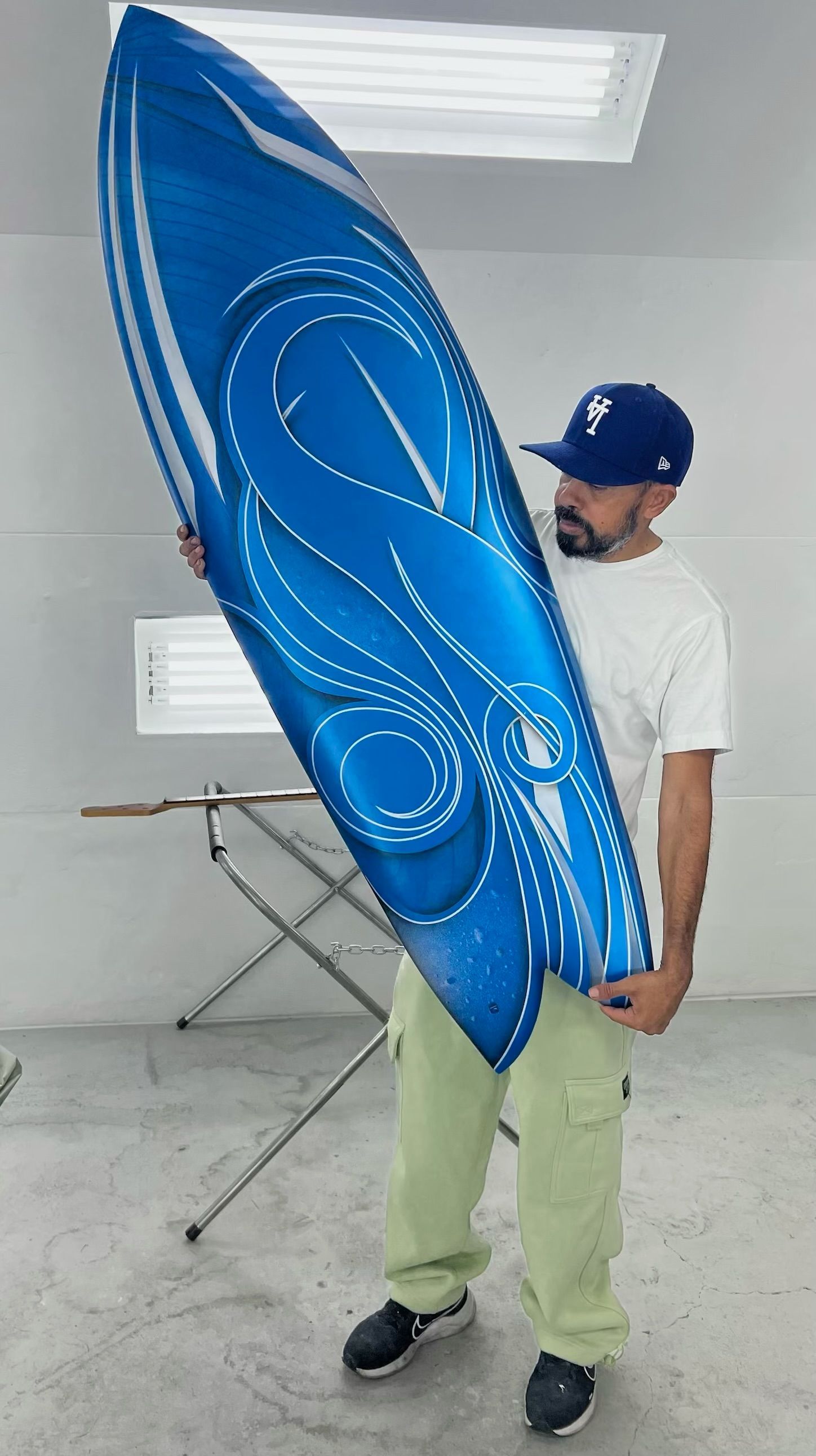 A man is holding a large blue surfboard in a room.