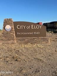 A city of eloy sign is sitting in the middle of a dirt field.