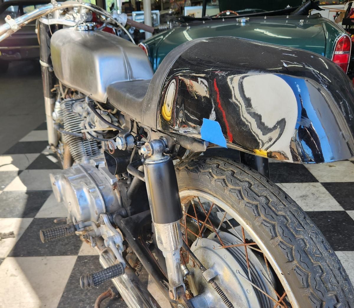 A motorcycle is sitting on a checkered floor next to a green car