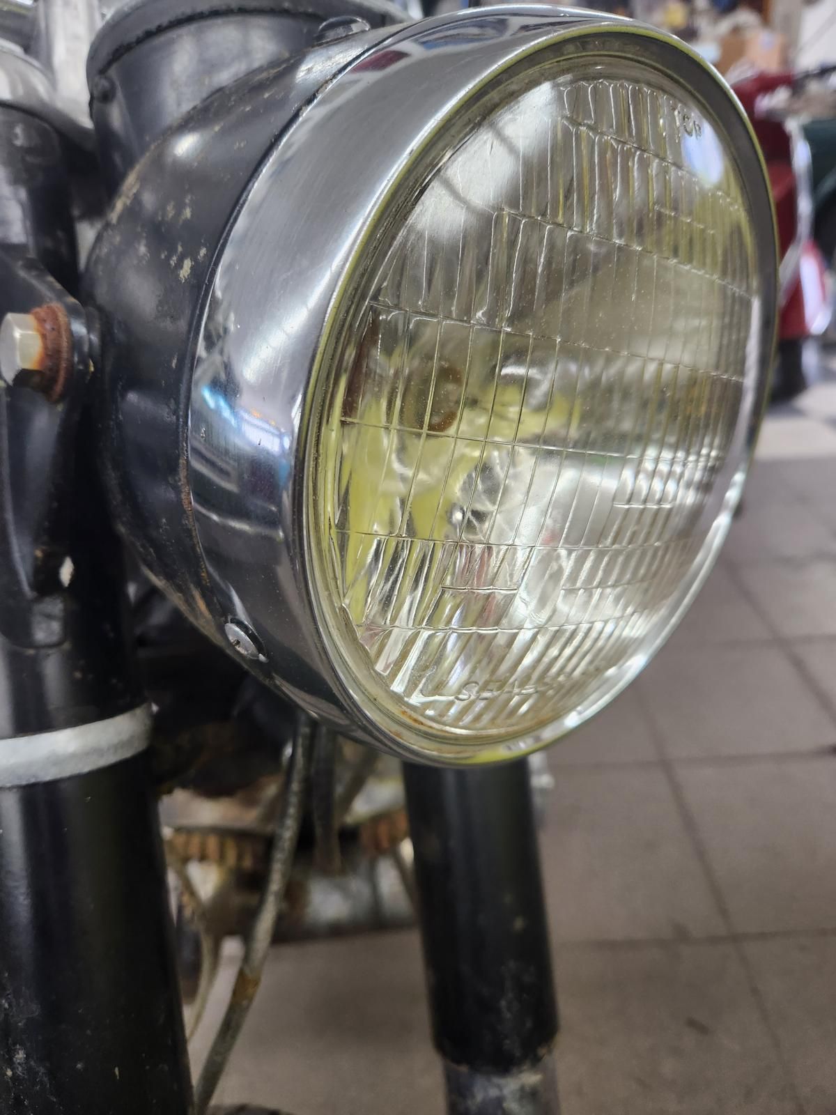 A close up of a motorcycle headlight on a tiled floor.