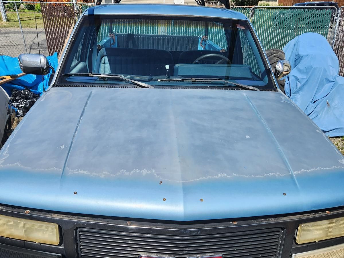 A blue gmc truck is parked in front of a fence.