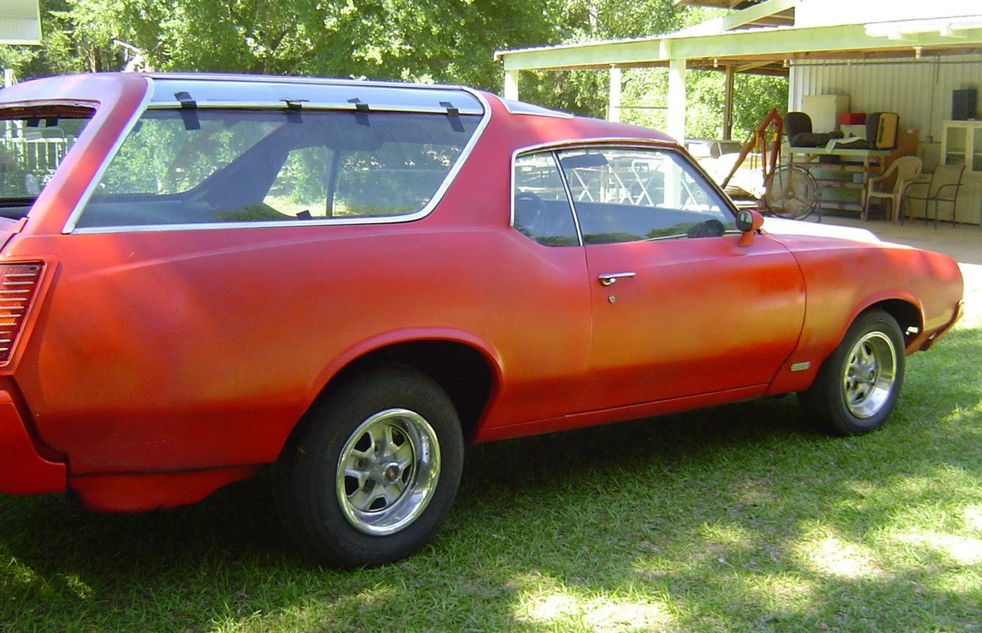 A red car is parked in the grass in front of a garage