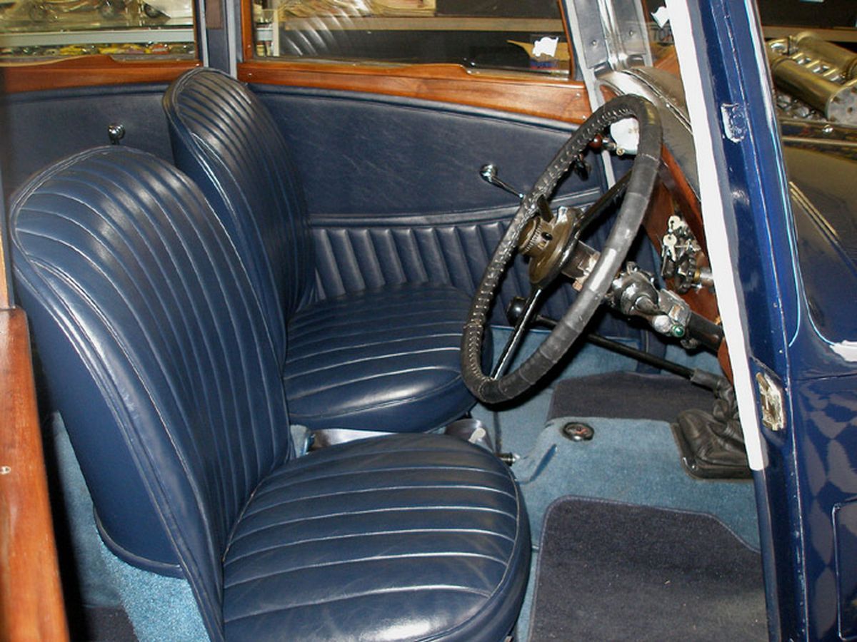 The inside of an old car with blue seats and a steering wheel