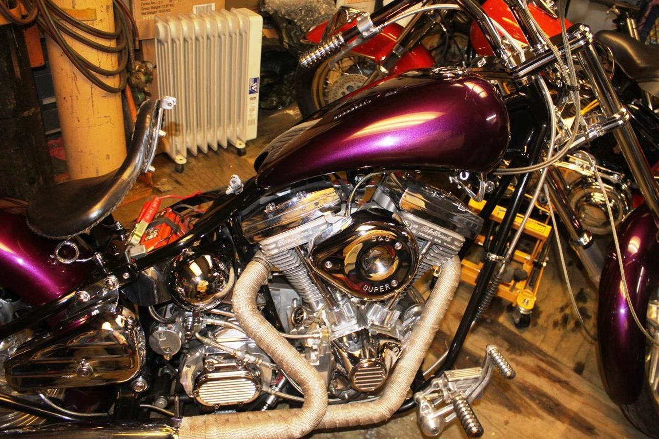 A purple motorcycle is parked in a garage next to a radiator