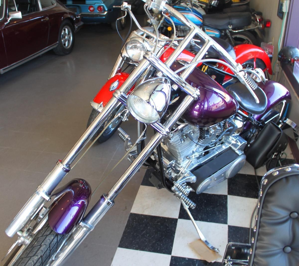 A purple motorcycle is parked in a garage next to a red car