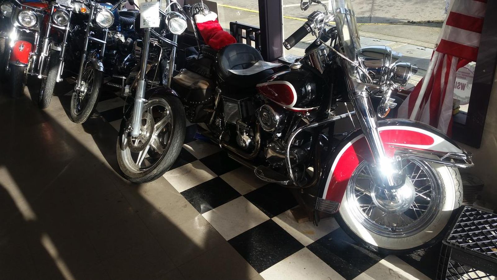 A row of motorcycles are parked on a checkered floor in a garage.