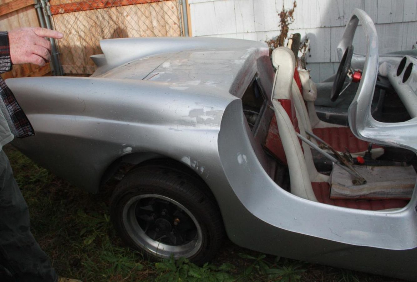 A man is pointing at a silver car in the grass