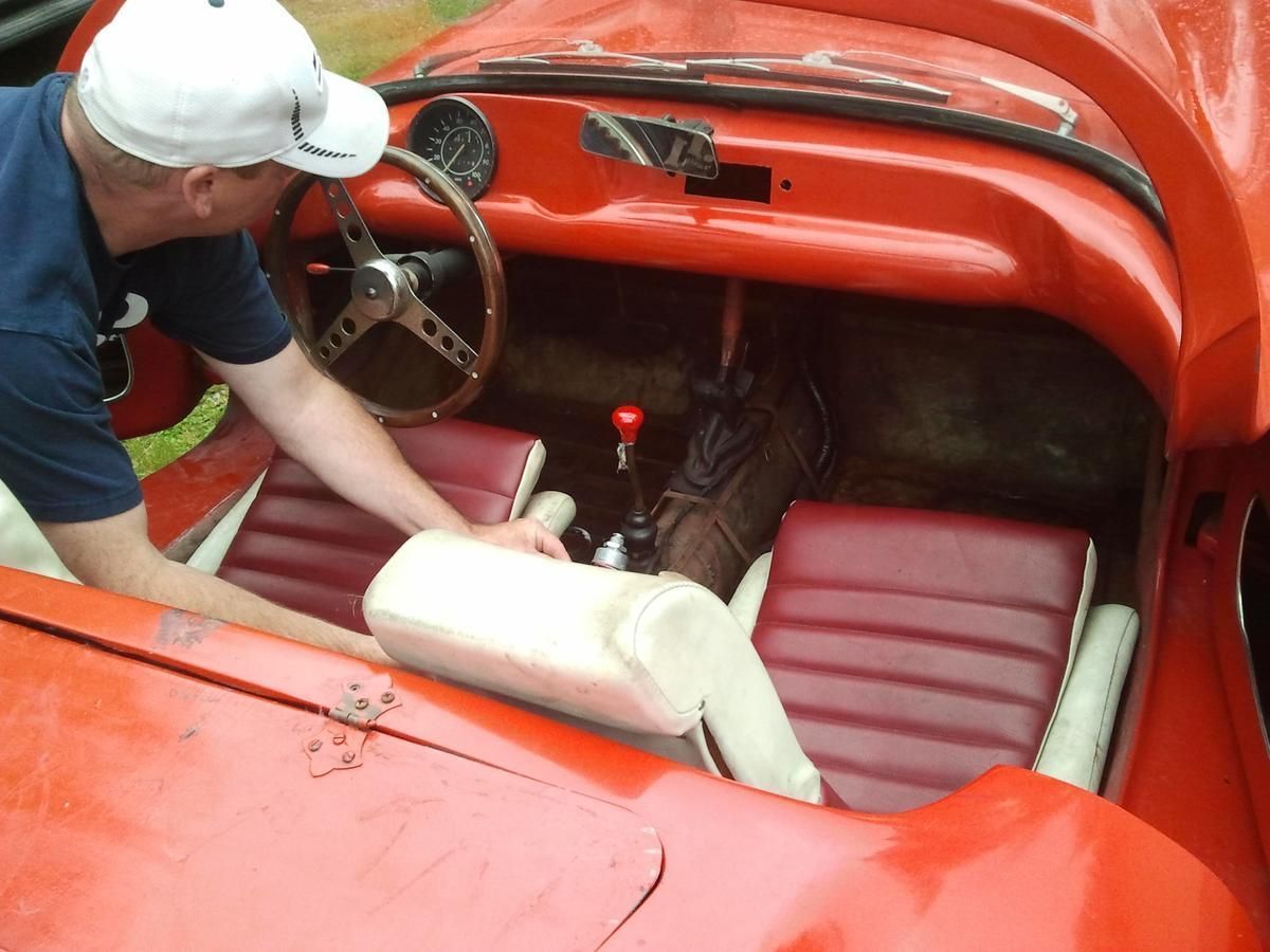 A man in a white hat is looking at the interior of a red car