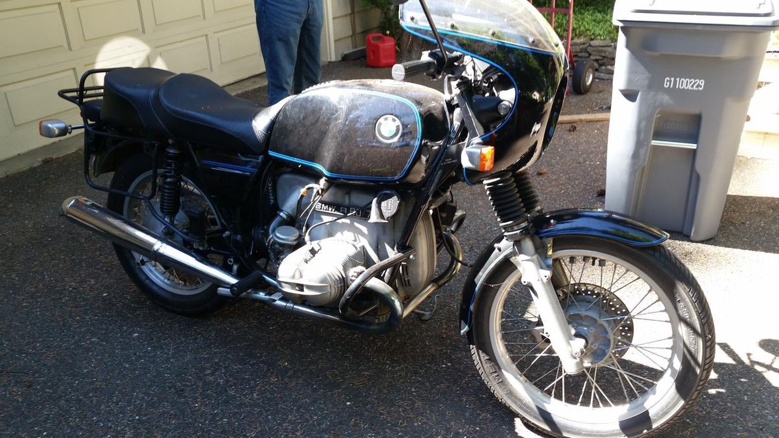 A motorcycle is parked in a driveway next to a trash can.