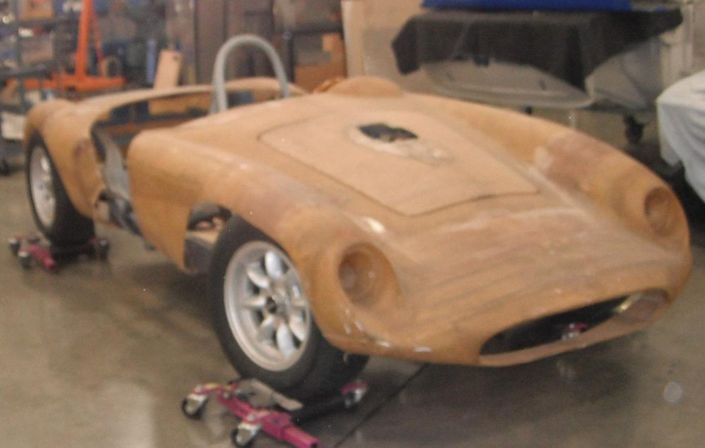 A wooden sports car is sitting on wheels in a garage