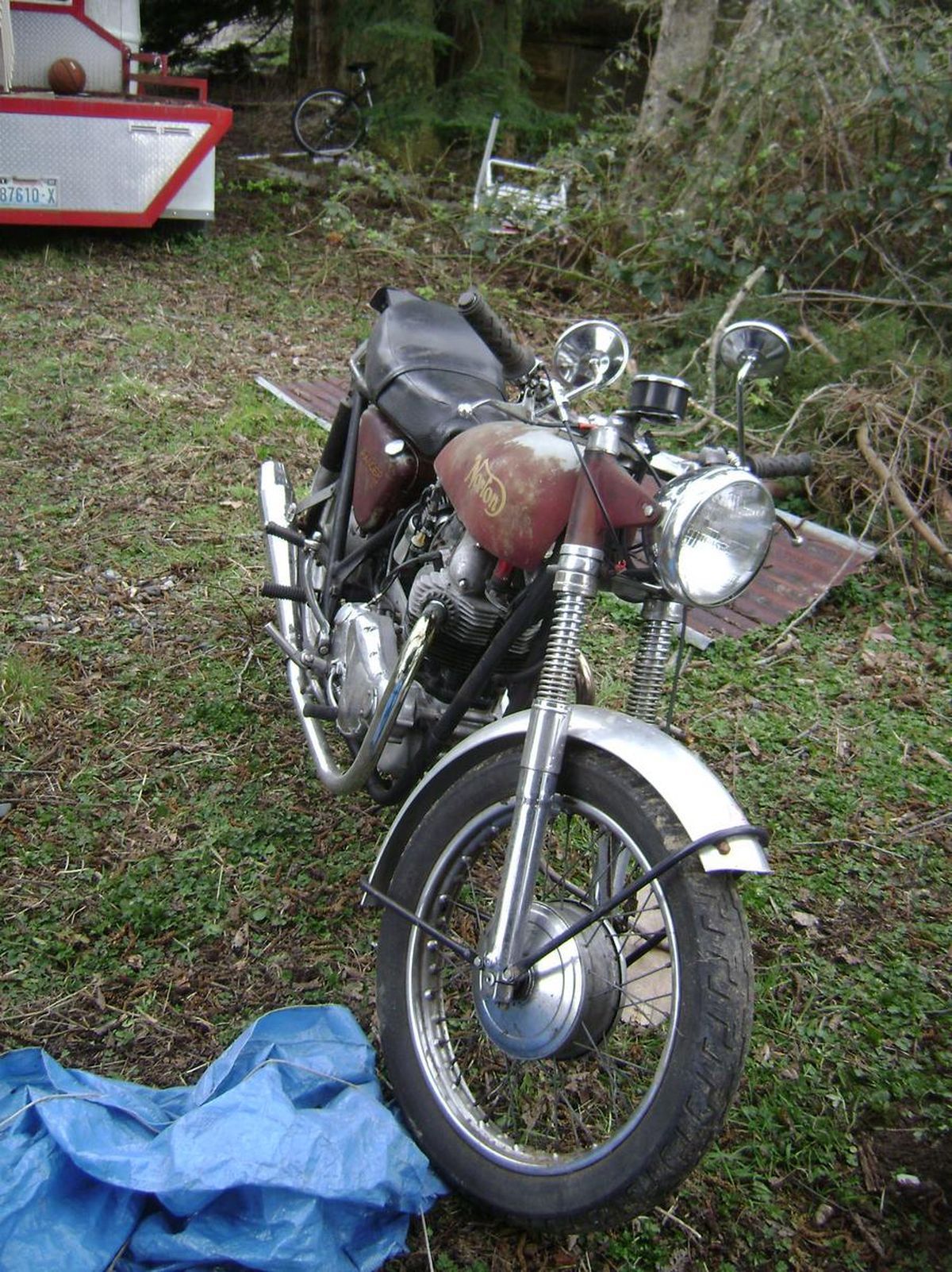 A motorcycle is parked in the grass with a blue tarp on the ground