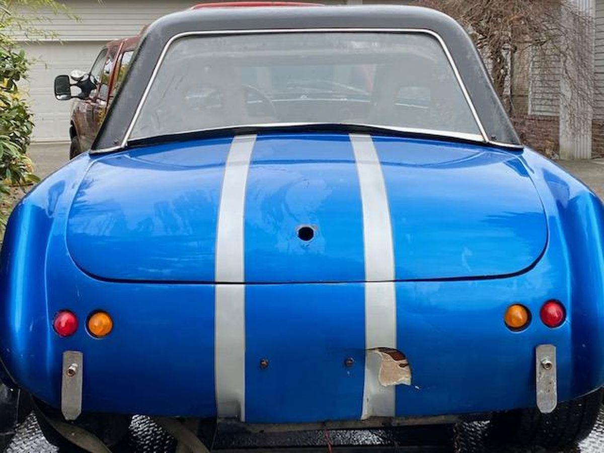 A blue car with white stripes on the back is parked in front of a garage.