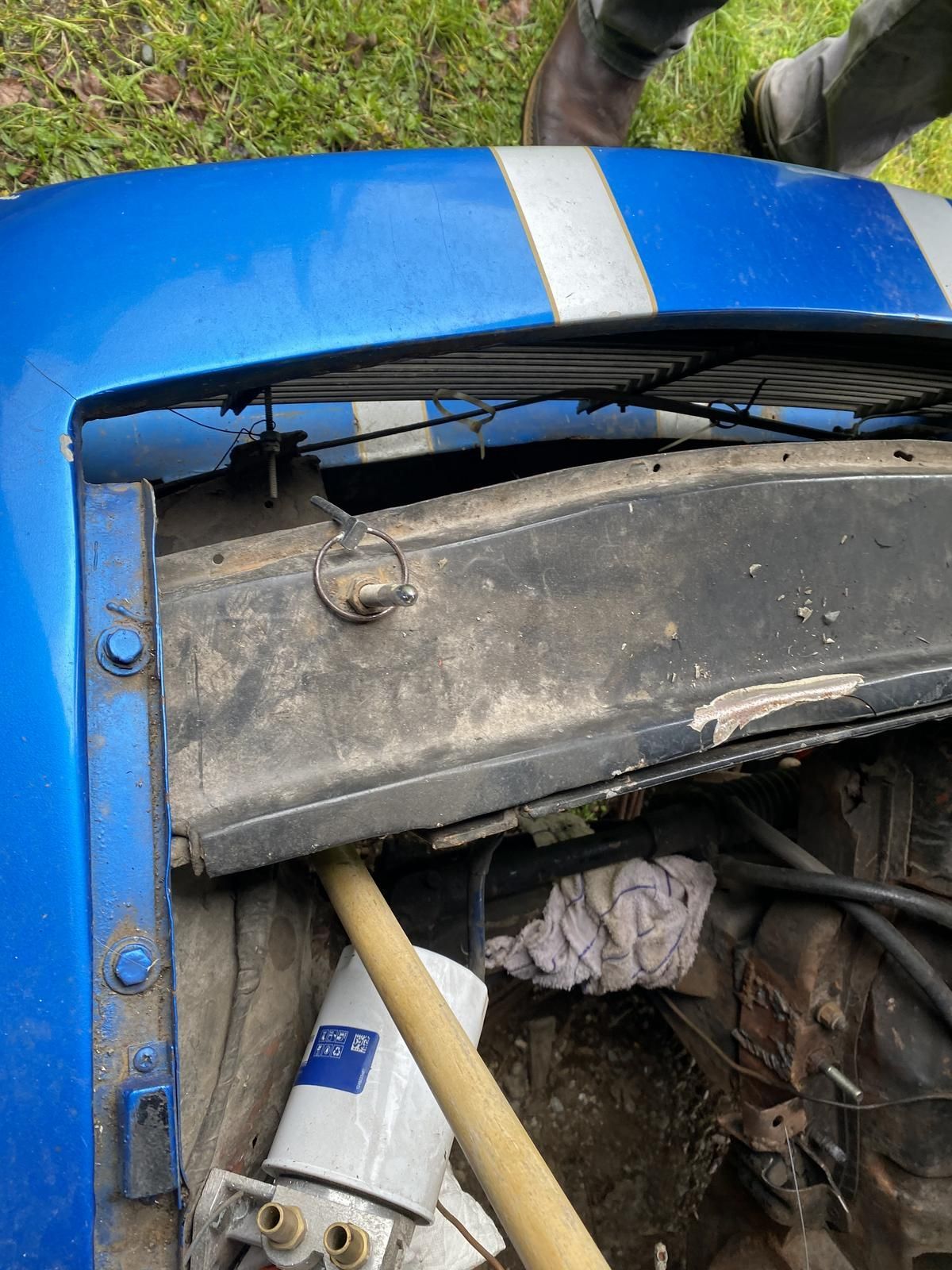 A person is standing next to a blue car with the hood open.