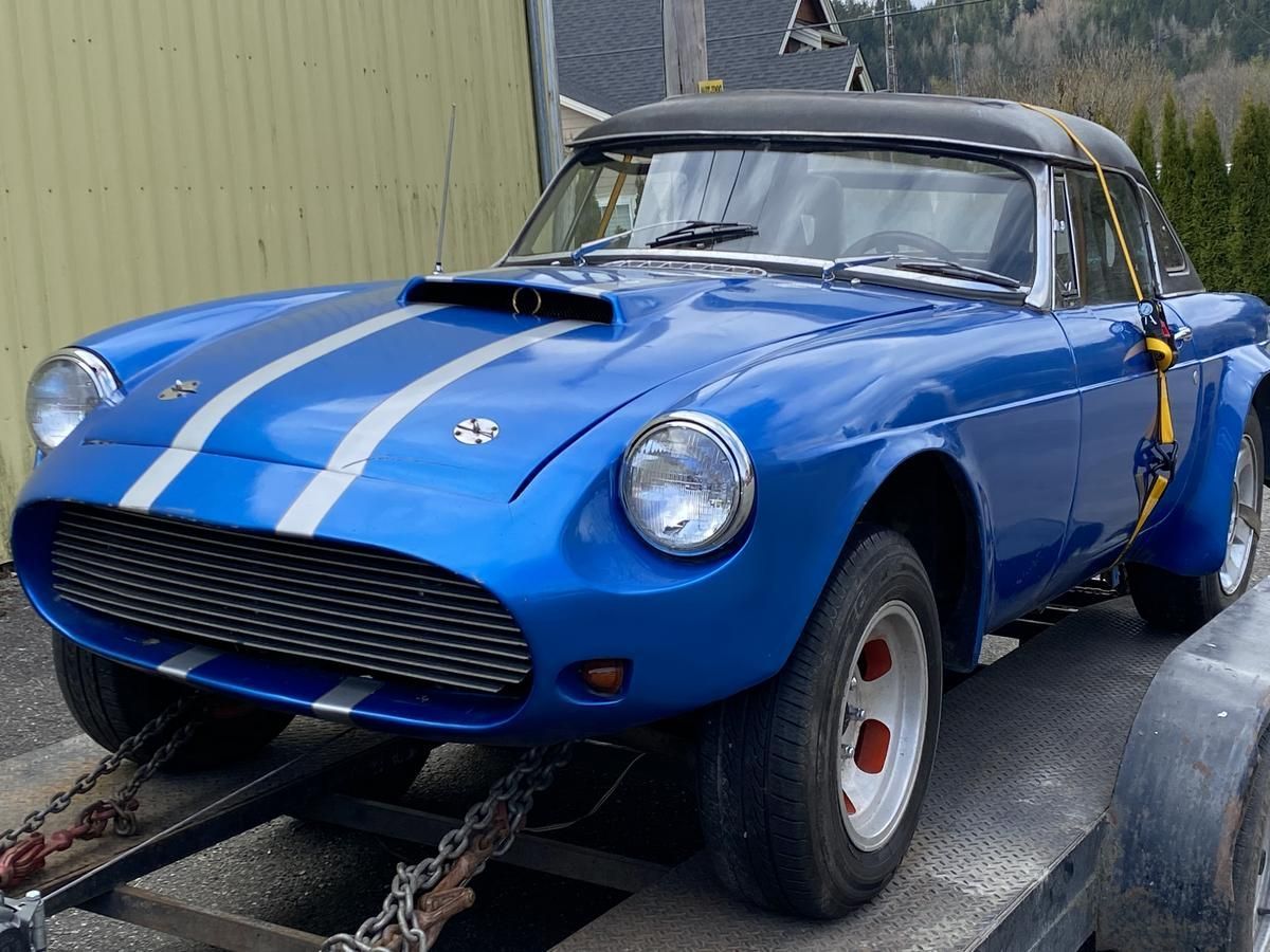 A blue car with white stripes is on a trailer