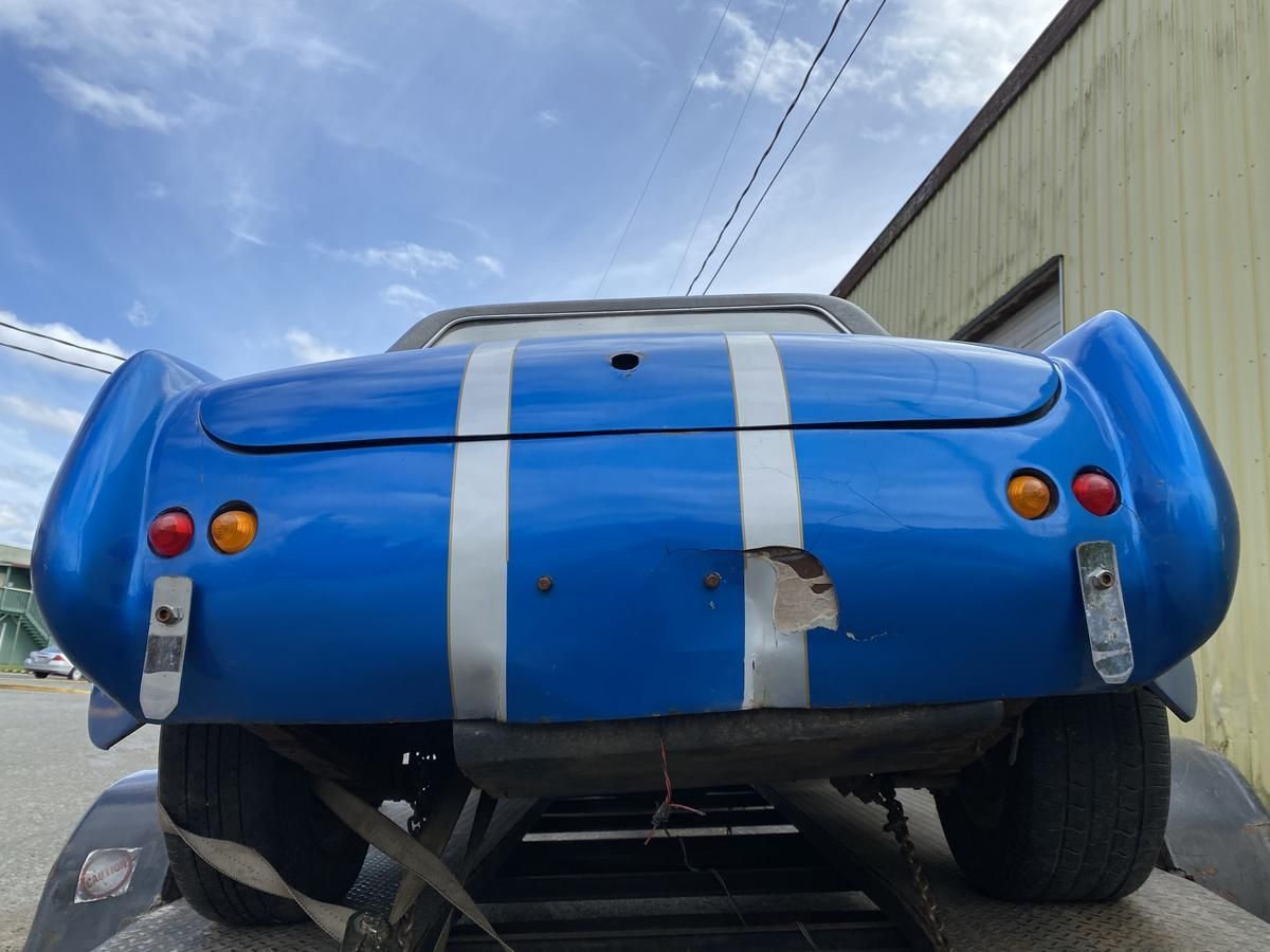 A blue car with white stripes on the back is parked in front of a building.