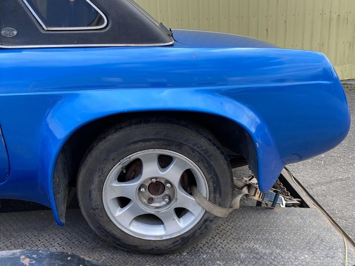 A blue car with a silver wheel is tied to a trailer.