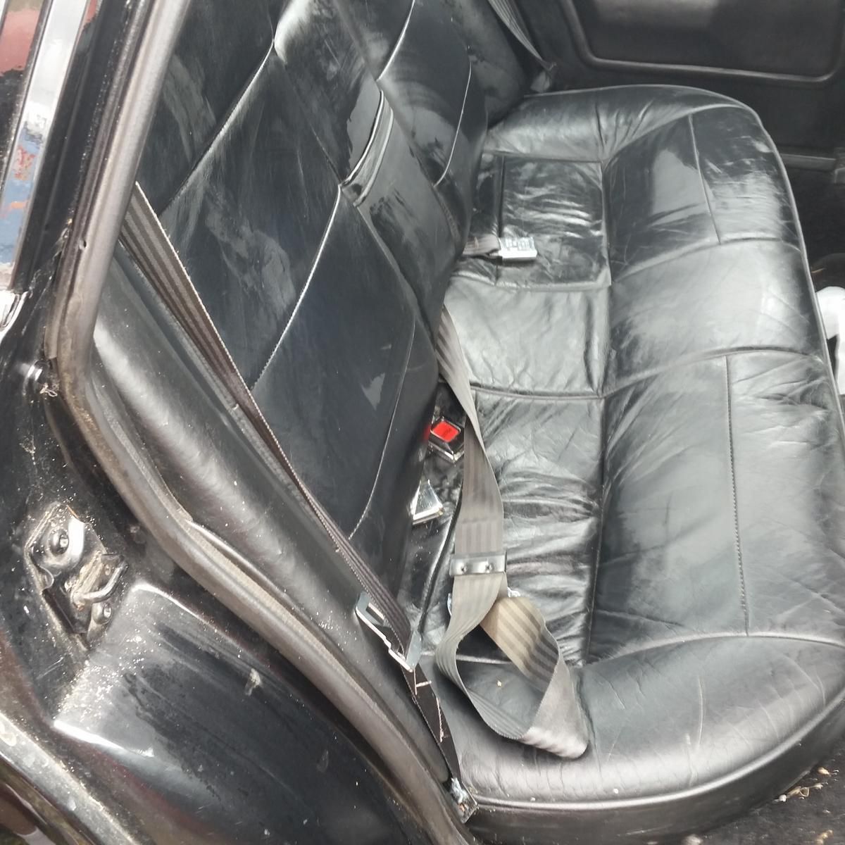 The back seat of a black car has a seat belt on it