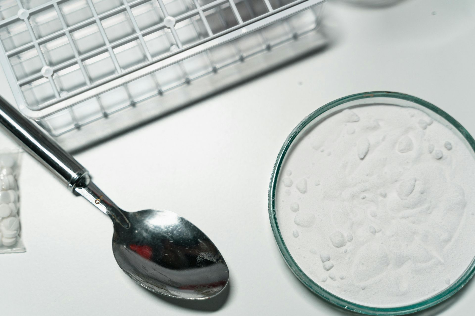 A spoon is sitting next to a petri dish on a table.