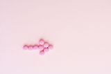 Pink pills in the shape of an arrow on a pink background.
