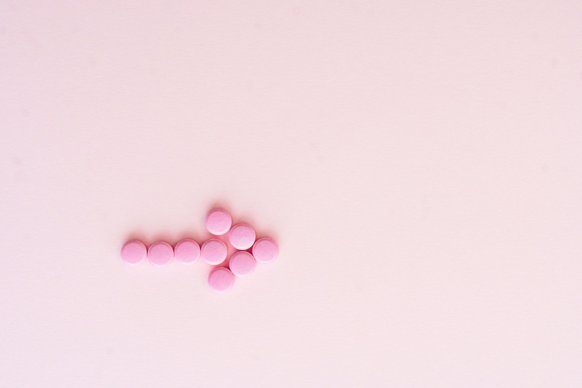 Pink pills in the shape of an arrow on a pink background.