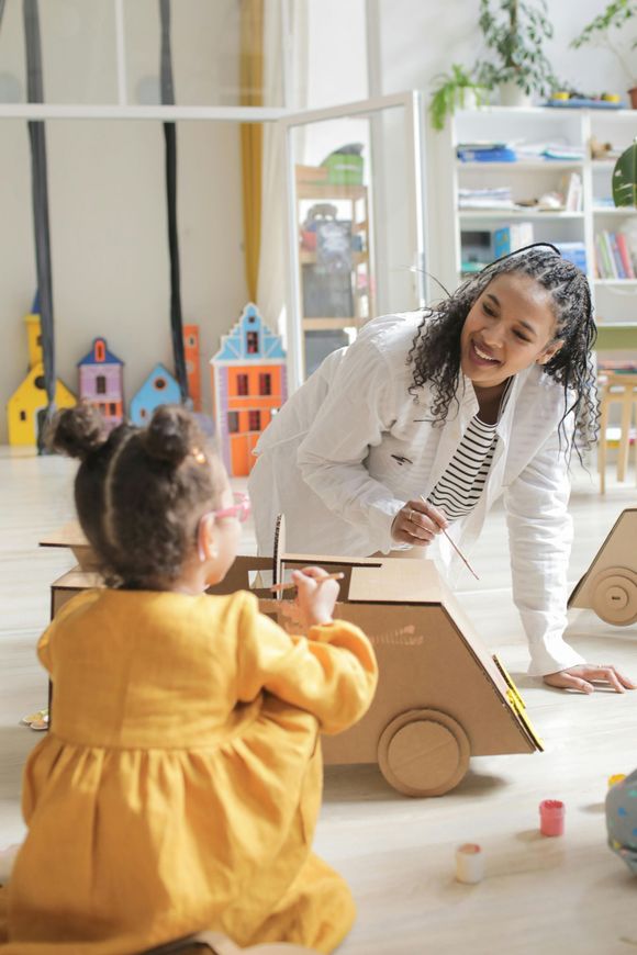 A doctor is talking to a little girl who is playing with a cardboard car.