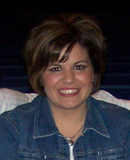 A woman wearing a denim jacket and necklace smiles for the camera