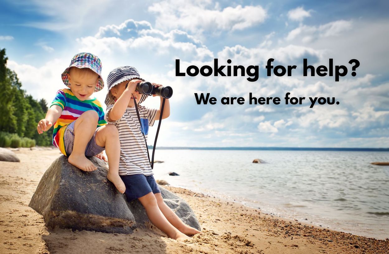 Two children are sitting on a rock on the beach looking through binoculars.