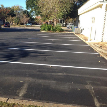 A paved parking lot with freshly painted white parking space lines next to a white building.
