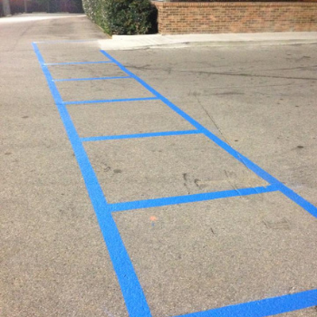 Blue rectangular outlines are painted on an asphalt parking lot surface, creating a series of marked parking spaces.
