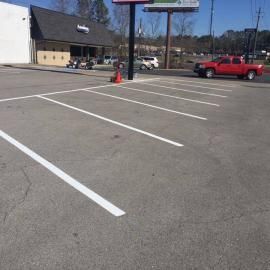 An empty parking lot with freshly painted white lines in front of a commercial building and a red pickup truck.