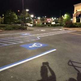 A night scene of a parking lot featuring blue and white painted accessible parking markings and cross-hatching.