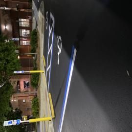 An accessible parking spot at night, featuring a blue-bordered space with a wheelchair symbol painted on the pavement.