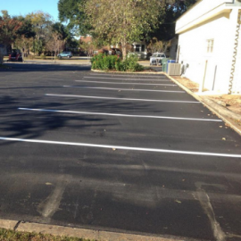 A freshly paved asphalt parking lot with white painted lines delineating empty parking spaces next to a white building.