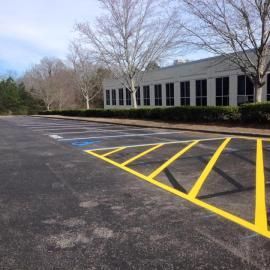 An empty parking lot with a handicap spot marked by blue paint and a yellow-striped no-parking zone in the foreground.