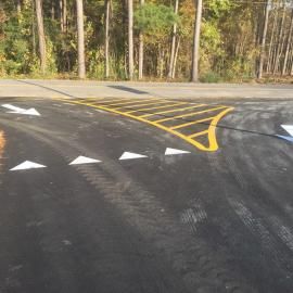Yellow road markings for a traffic island and white yield triangles on asphalt pavement at a T-junction.
