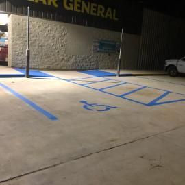 A Dollar General store parking lot at night, featuring a blue-painted accessible parking space with an access aisle.