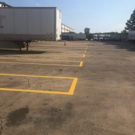 A large, outdoor shipping yard featuring several parked semi-trailers and yellow-painted parking space markings.