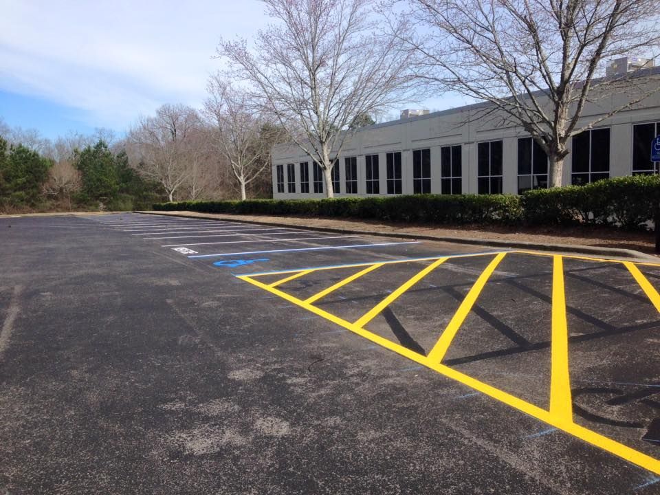 Empty parking lot with a yellow-striped buffer zone and a blue-painted accessible parking spot beside a building.
