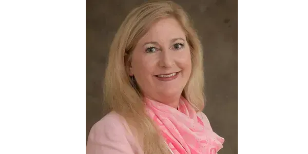 A woman in a pink jacket and pink scarf is smiling for the camera.