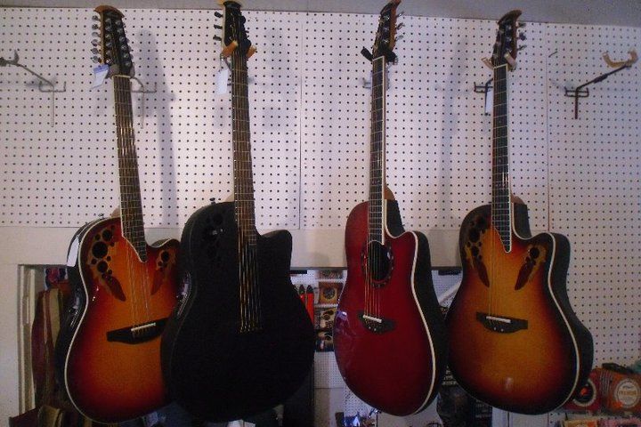 Four acoustic guitars hanging on a wall, in sunburst, black, red, and sunburst finishes.