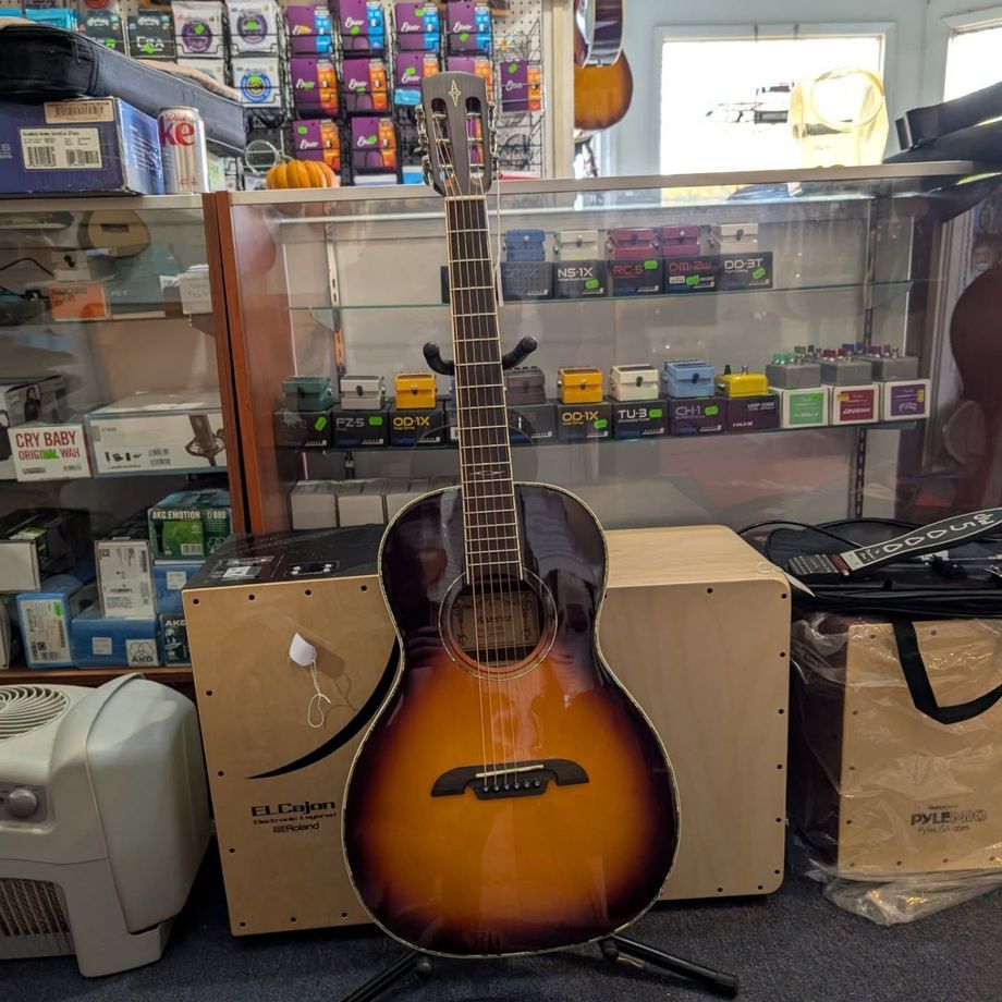 Sunburst acoustic guitar displayed in a music shop with boxed equipment behind it