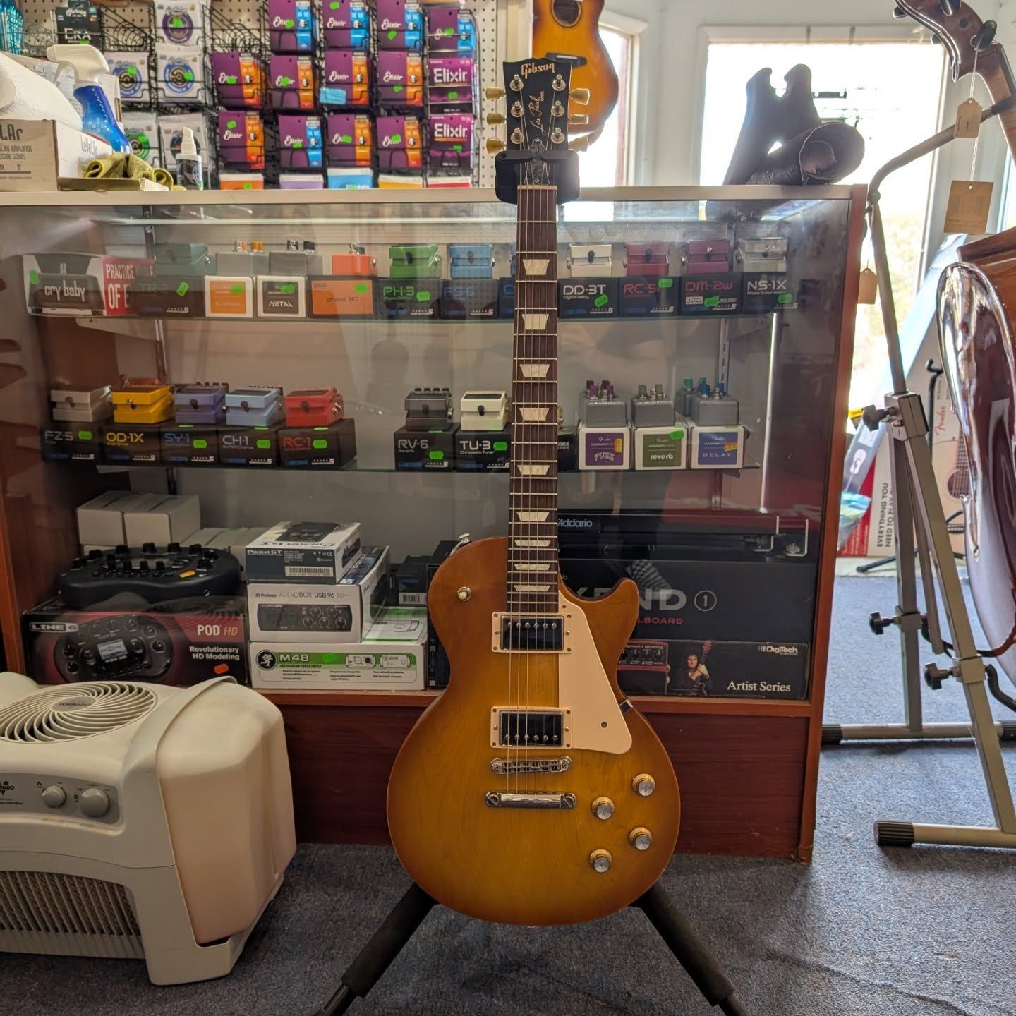Sunburst electric guitar on a stand in a music shop, with gear and amp displays behind it.