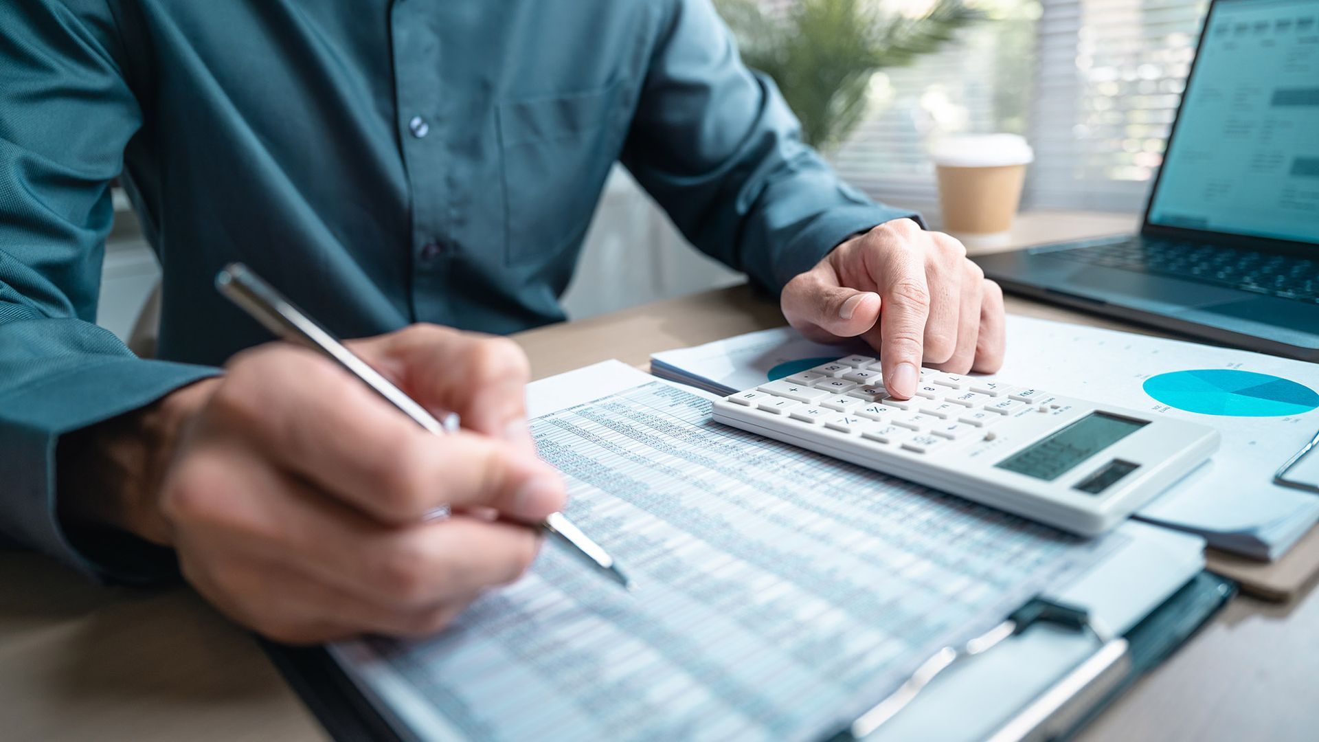 Person in a blue shirt using a calculator while reviewing financial documents at a desk.
