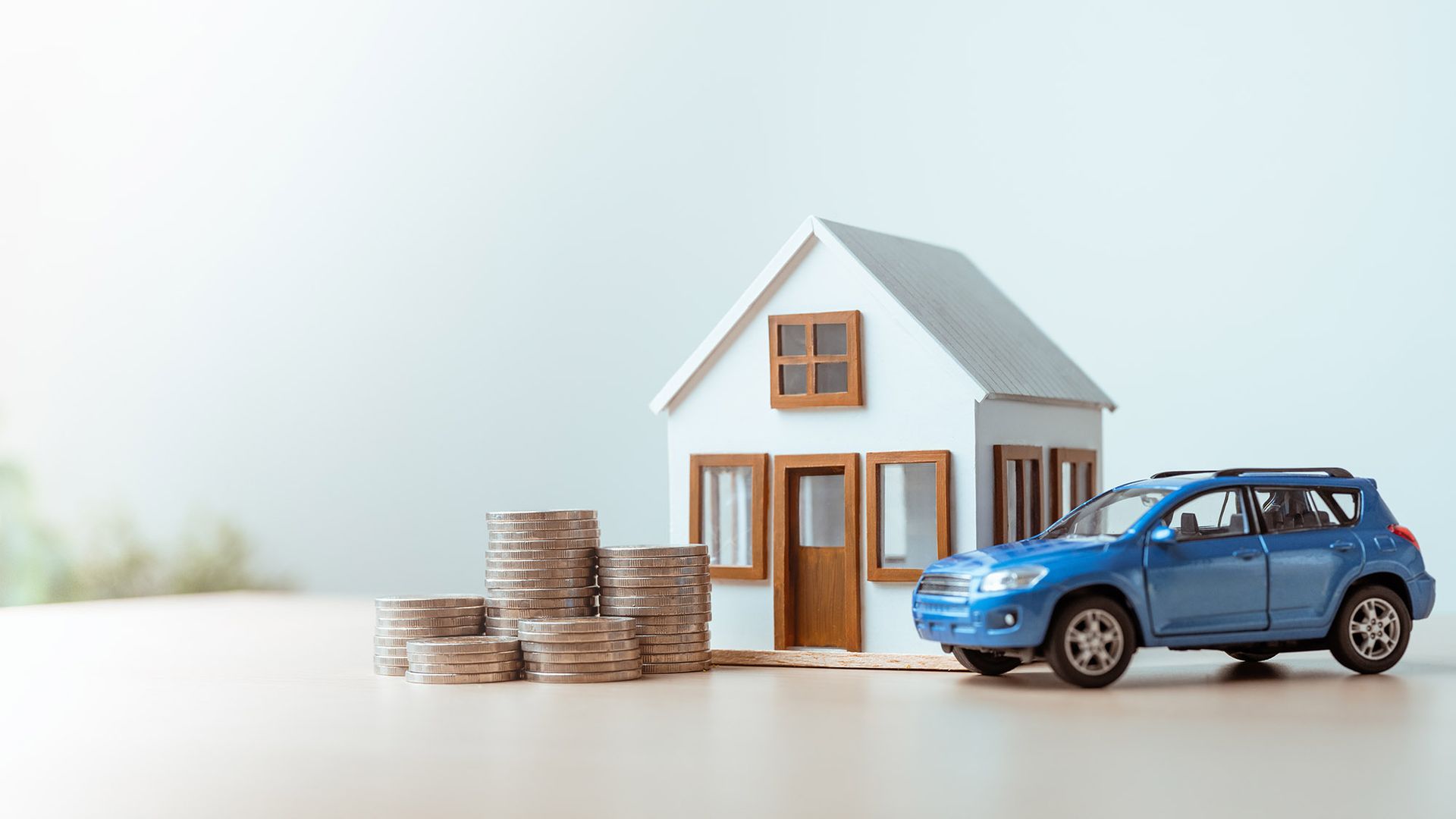 Toy house, car, and stacks of coins, representing savings and property.