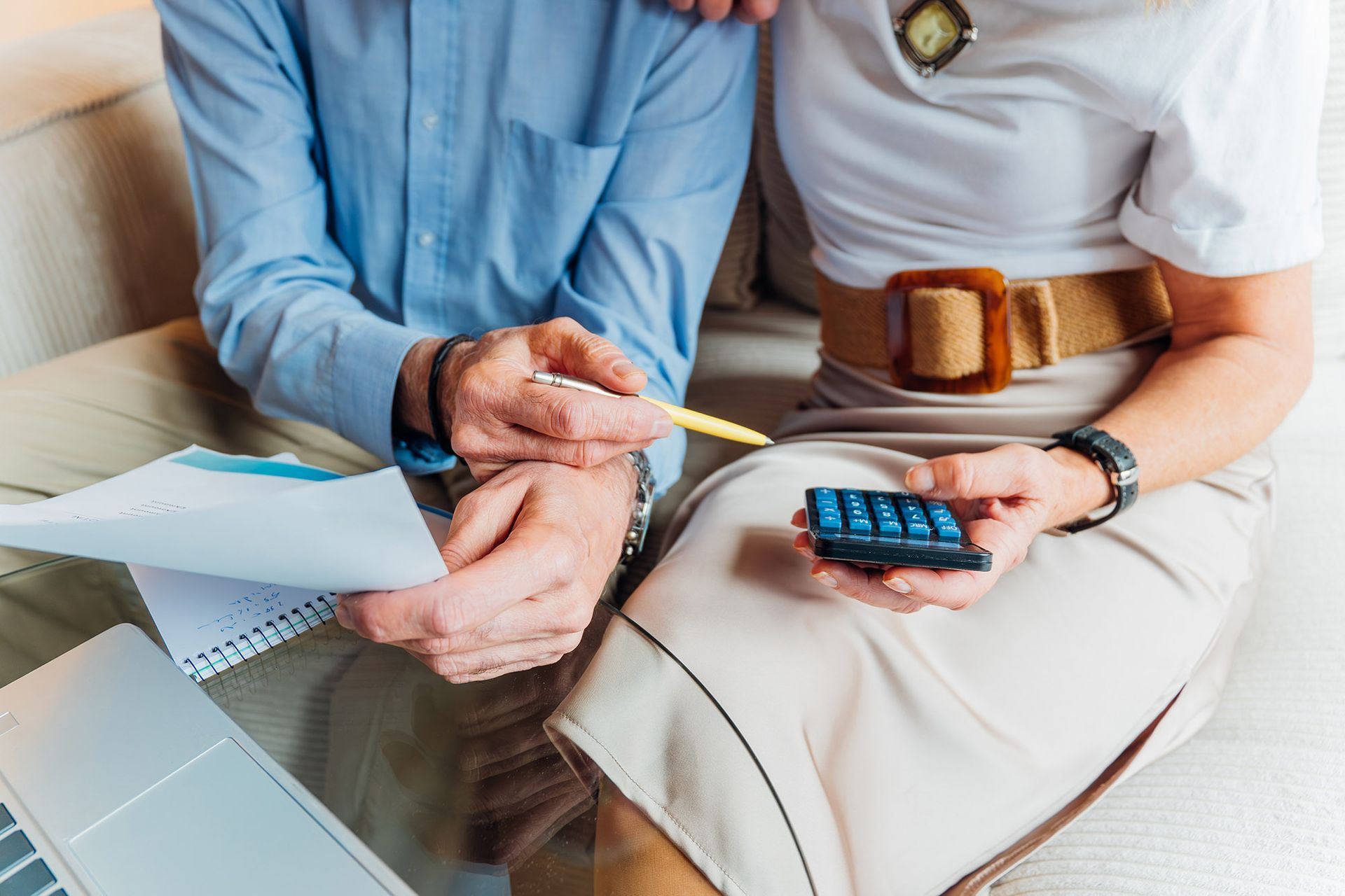 Two people reviewing financial documents with a calculator and pen on a couch.