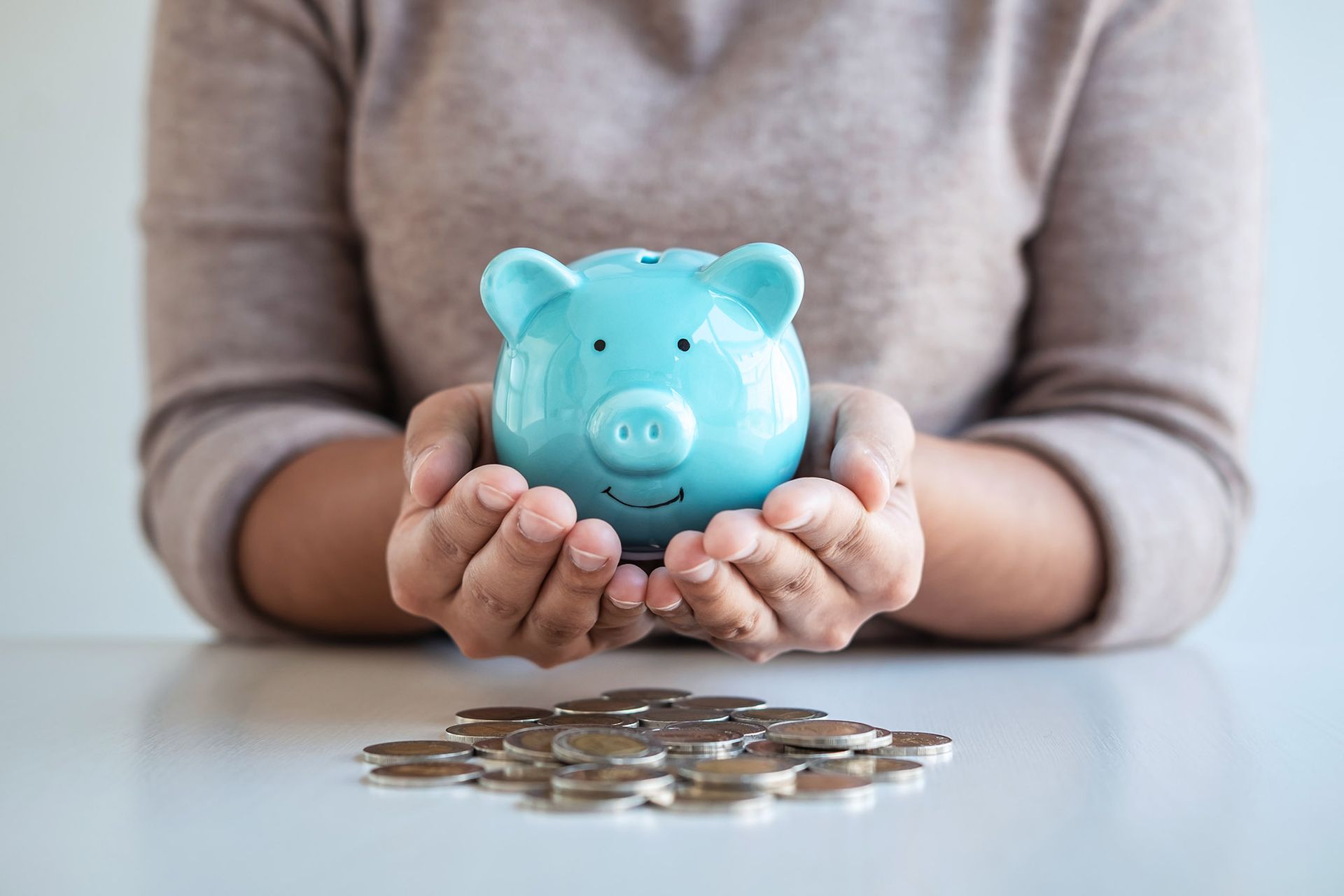 Hands cupping a blue piggy bank, resting above a pile of coins.