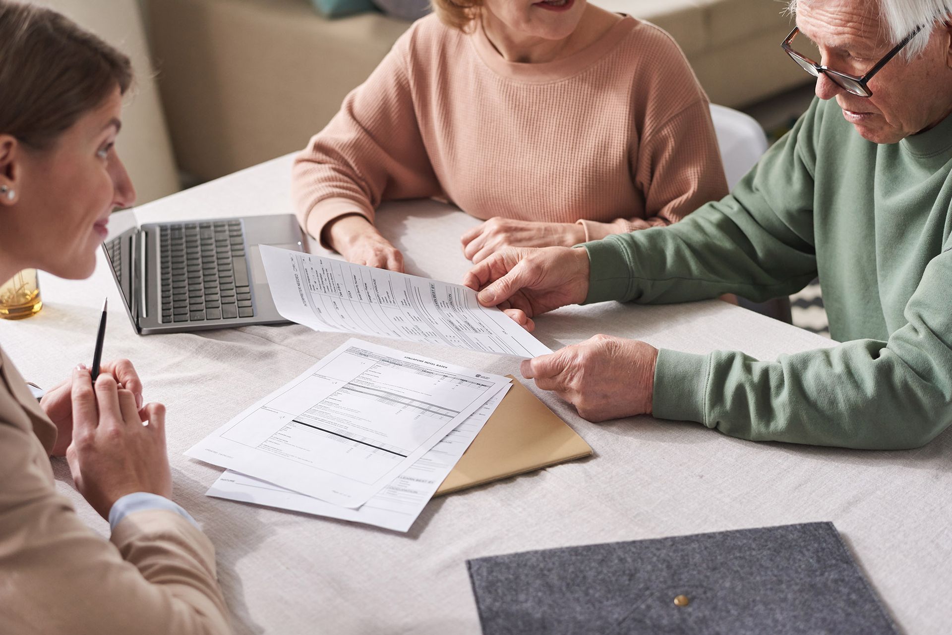 Woman assisting a senior couple with paperwork at a table; documents, laptop.