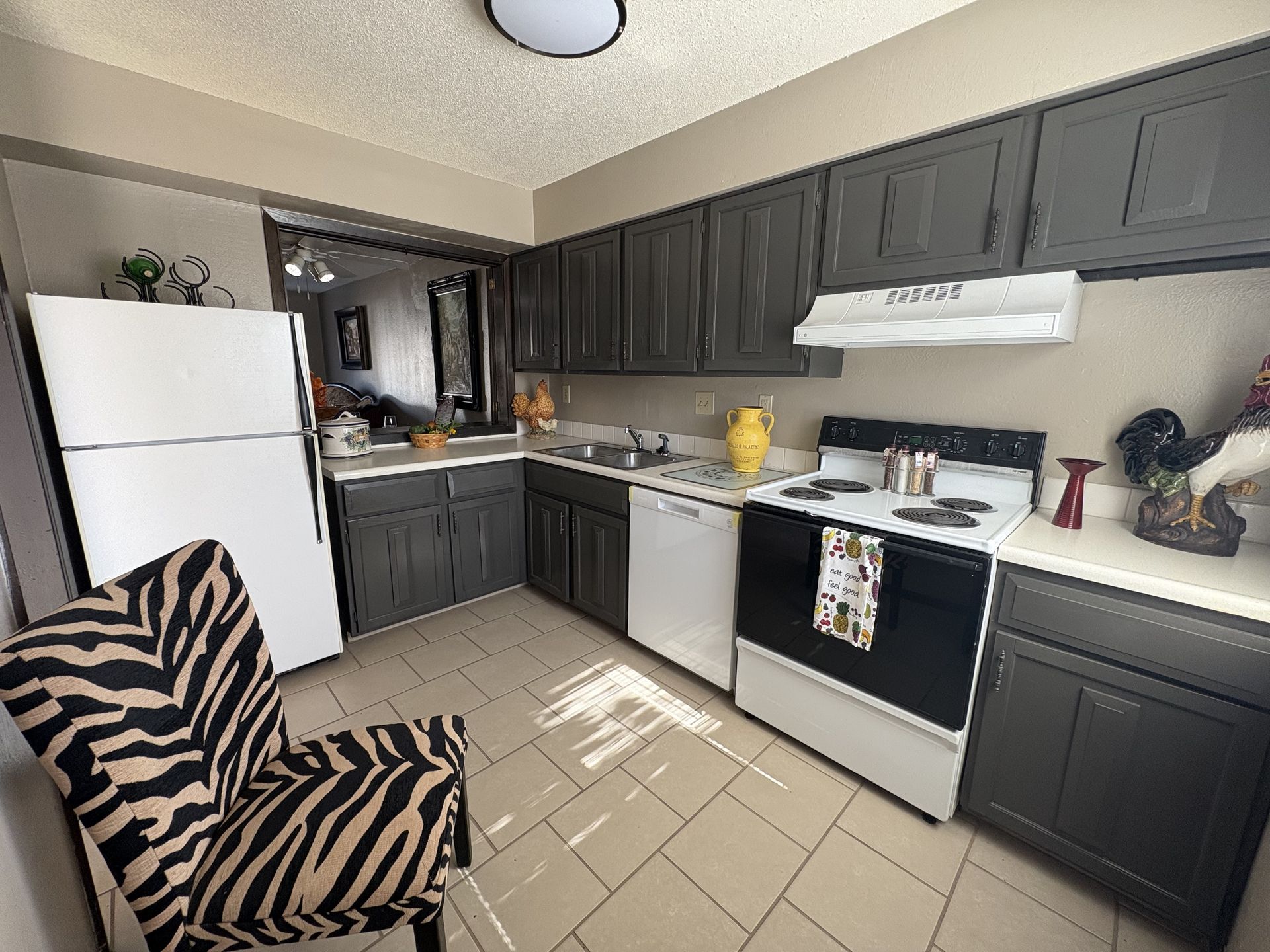 Kitchen with dark gray cabinets, white appliances, and a zebra-print chair.