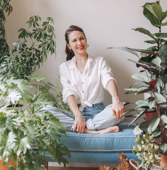 Sally Flower smiling on a couch surrounded by plants